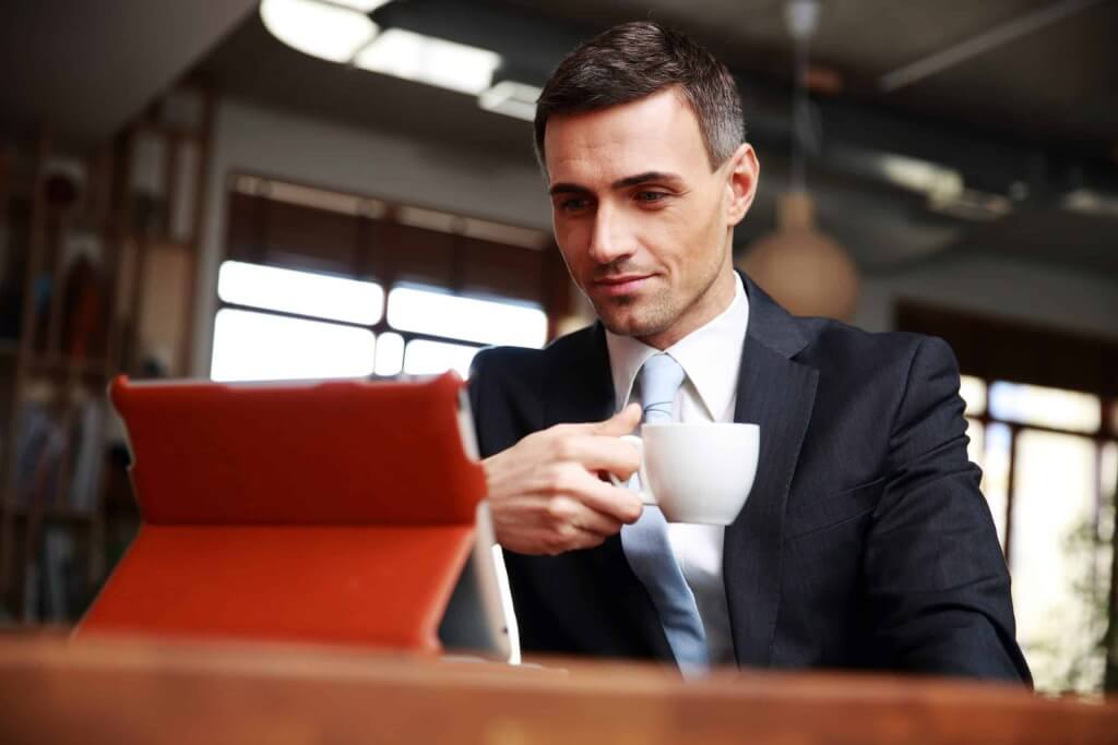 Geschäftsmann im Anzug mit Kaffee am Tablet, Steuerberatung Wien, individuelle Steuerstrategie