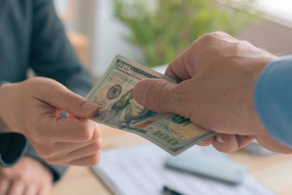 Hand übergibt 100-Dollar-Schein an andere Person, Fokus auf Beratung und Steueroptimierung
